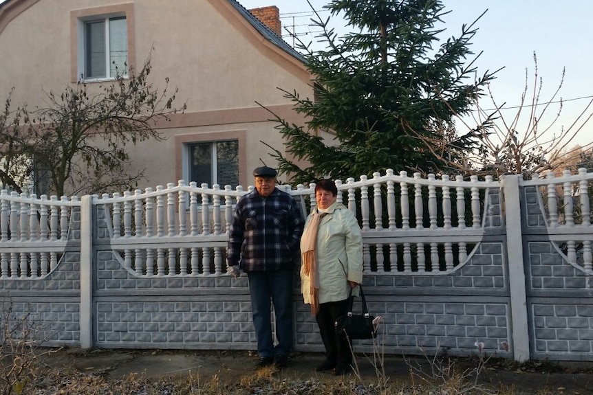 Elderly couple posing for a photo in front of a grey and white fence