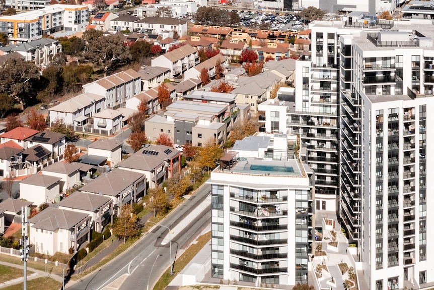 An aerial view of apartments and townhouses, with hills and scrub in the background.