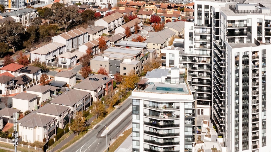 An aerial view of apartments and townhouses, with hills and scrub in the background.