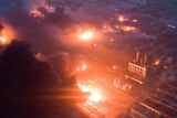 Overhead shot of fire blazing and smoke billowing in front of a night sky at the pesticide plant.