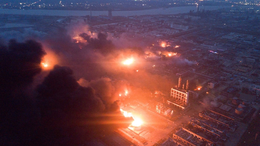 Overhead shot of fire blazing and smoke billowing in front of a night sky at the pesticide plant.