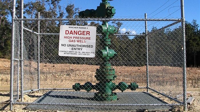 Large green well head sticking out of the ground, surrounded by chainlink fence topped with barbed wire