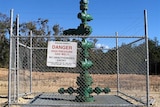 Large green well head sticking out of the ground, surrounded by chainlink fence topped with barbed wire