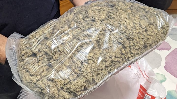 A police officer handles a large vacuum-sealed bag containing cannabis.