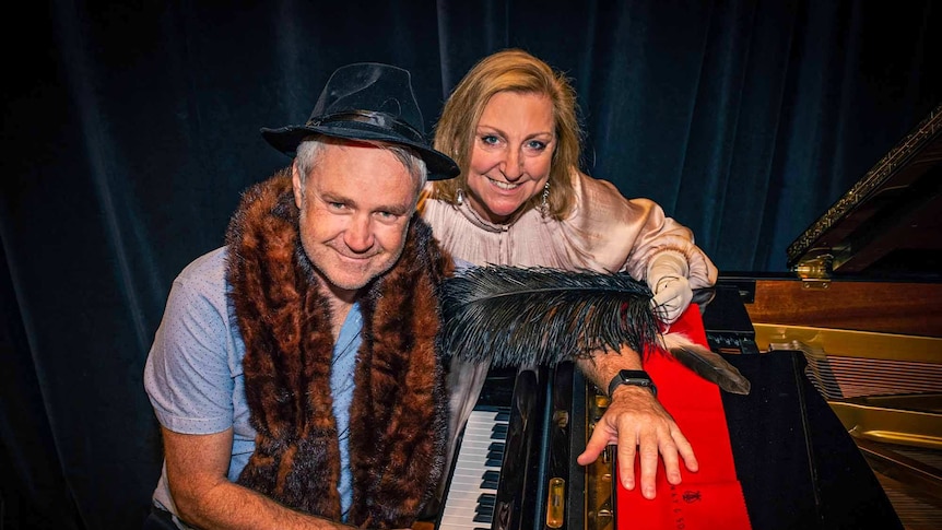 Jules Schiller and Sonya Feldhoff leaning over the keyboard of a grand piano with velvet curtains in the background.