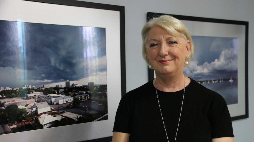 A woman stands in front of a photo of Darwin city.