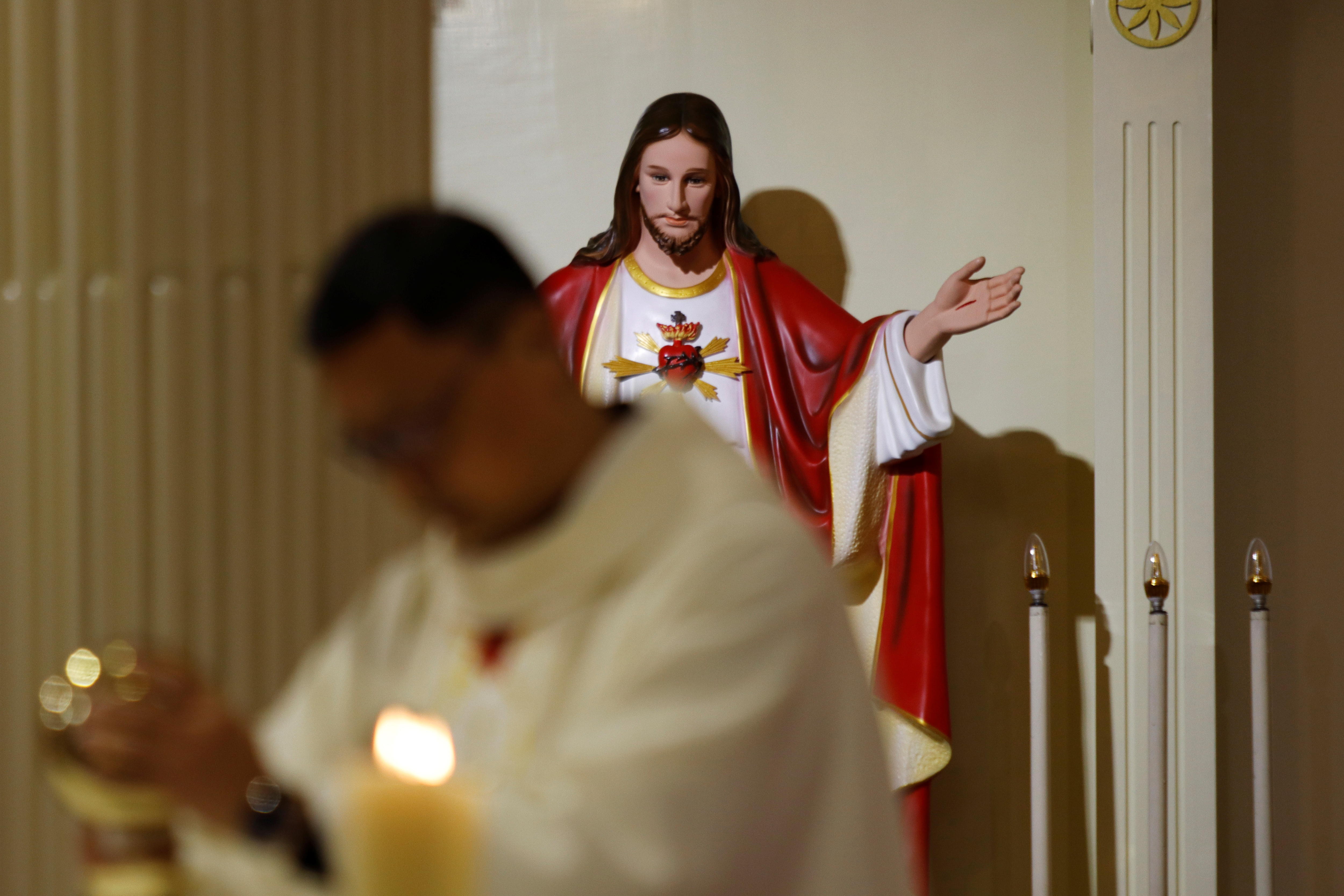 Uma estátua de Jesus Cristo está atrás de um padre conduzindo uma missa em uma igreja.