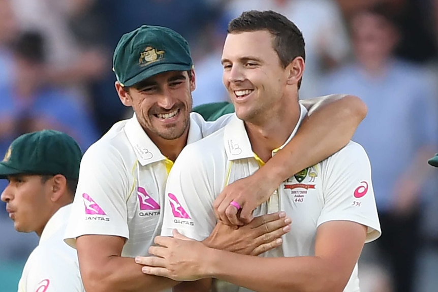 Australian fast bowler Mitchell Starc hugs teammate Josh Hazlewood from behind during a Test match.