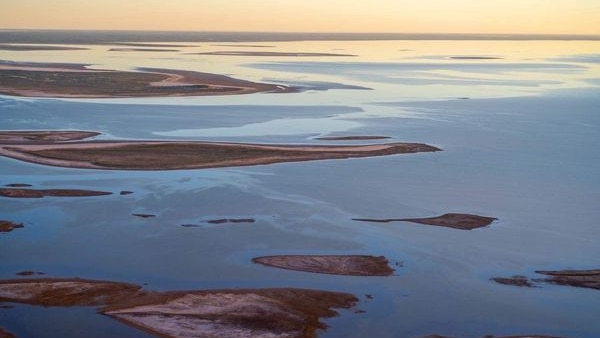 Water in the salt lake Kati Thanda-Lake Eyre on sunset glows in hues of yellow, pink and blue.