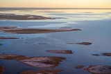 Water in the salt lake Kati Thanda-Lake Eyre on sunset glows in hues of yellow, pink and blue.
