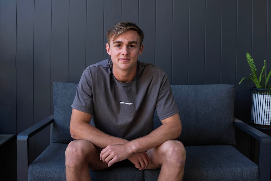 A young football player smiling at the camera with a red AFL football in his hands.