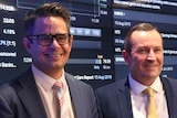 Wyatt and McGowan standing in front of a financial results board.