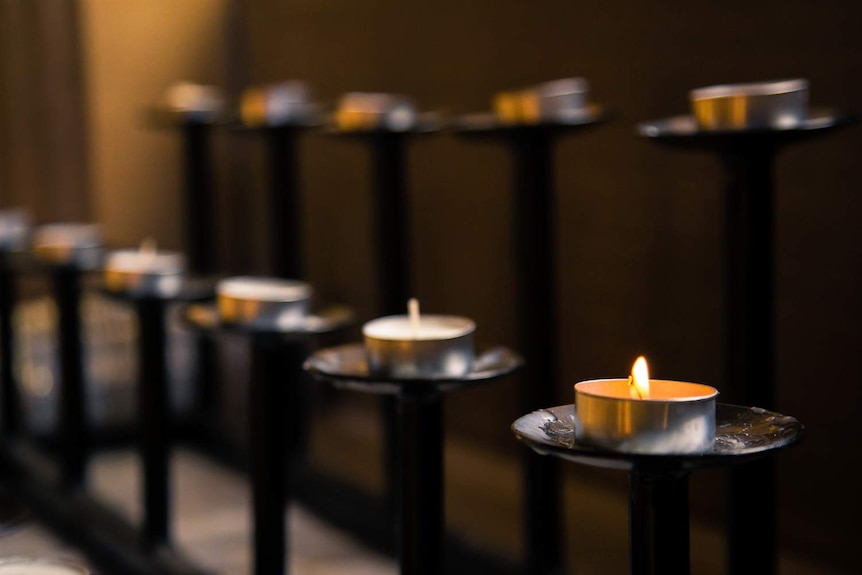 A candle lit in a row of lights inside a church.