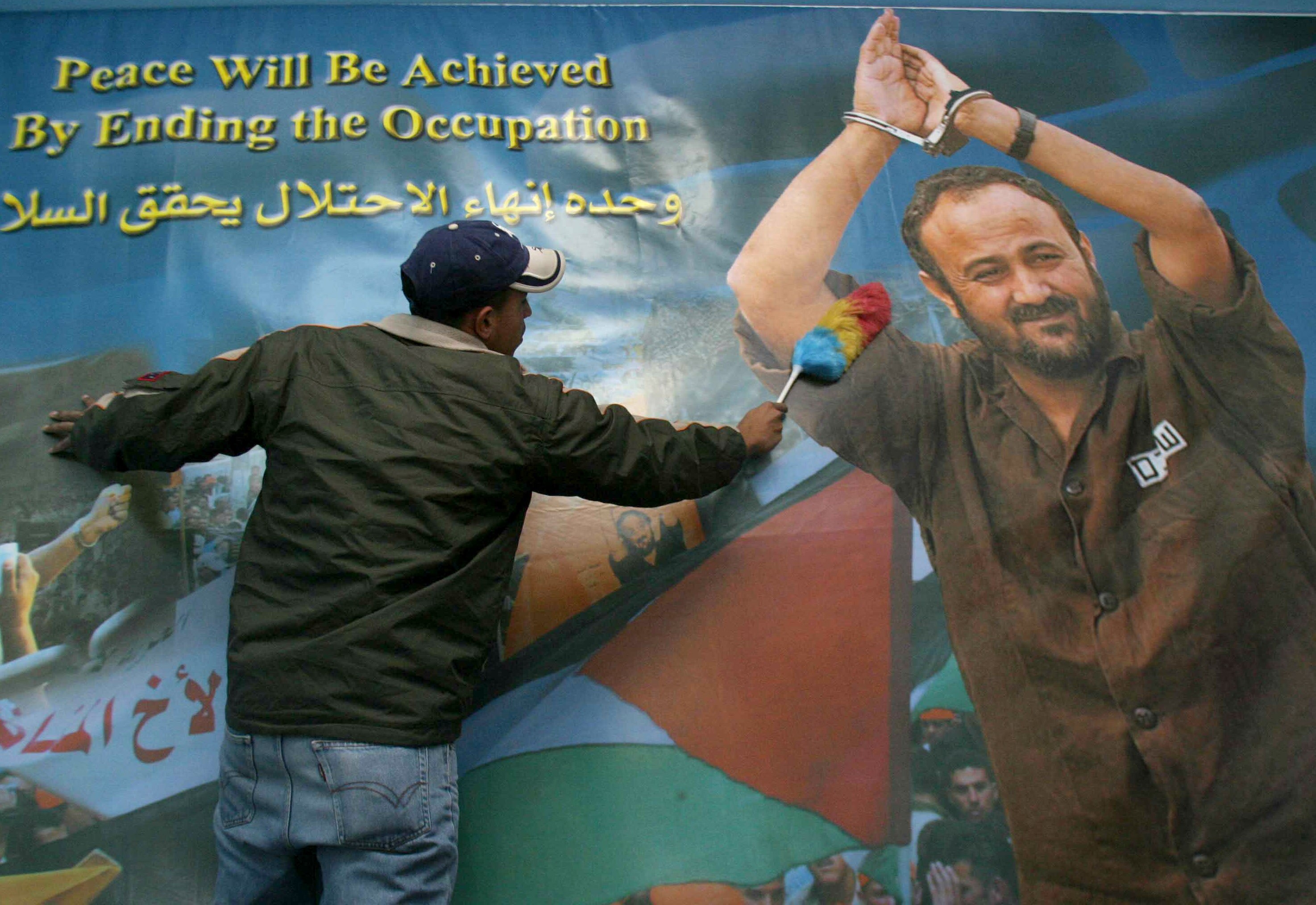 A man seen dusting a giant poster of Barghouti with the words "Peace will be acheived by ending the occupation".