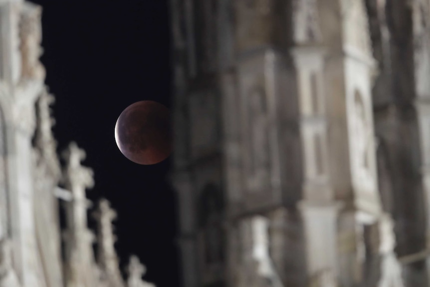 The moon is seen through spires of the Duomo gothic cathedral during a complete lunar eclipse.