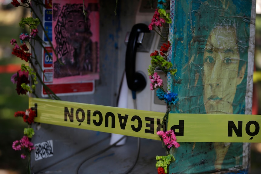 Flowers, danger tape and worn pictures of Lesvy Berlin Osorio mark the phone booth where her body was found in March.