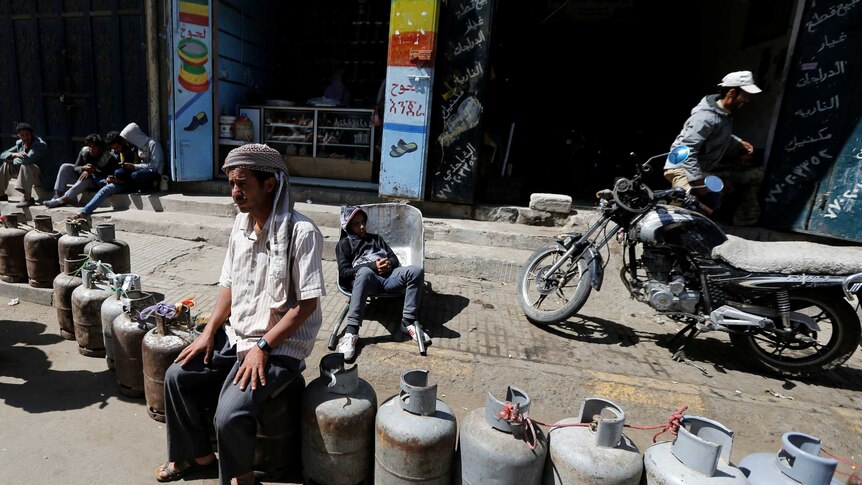 A man sits on a line of gas bottles in a street in Yemen.
