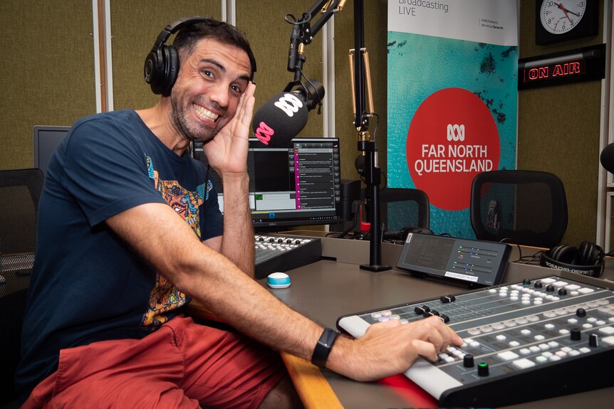 a man in a radio studio smiles while wearing headphones