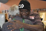 Stanley Warrie wearing a black hat and brown shirt hugs a friend after reacting to the native title judgment.