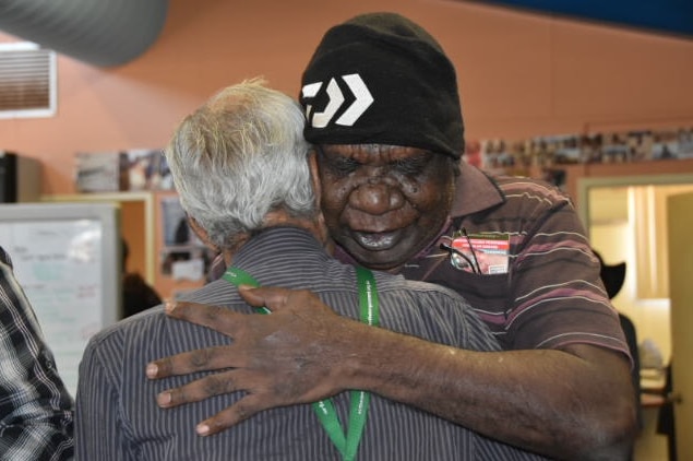 Stanley Warrie wearing a black hat and brown shirt hugs a friend after reacting to the native title judgment.