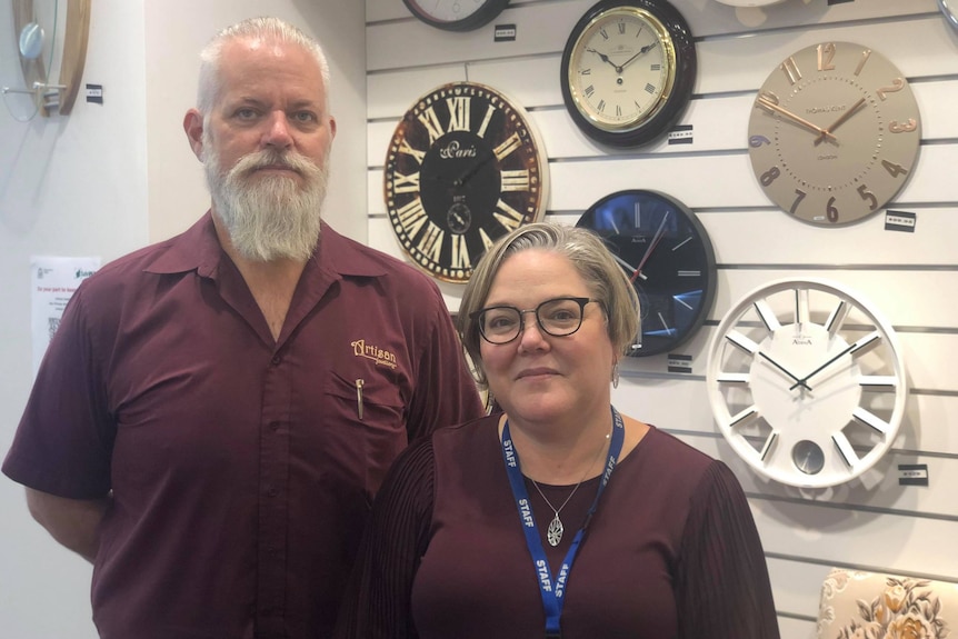 Man and woman wearing dark red shirts standing in front of wall of clocks