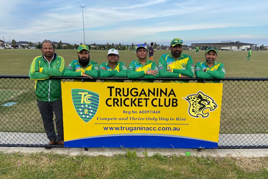Six committee members of the Truganina Cricket Club standing in front of their club banner