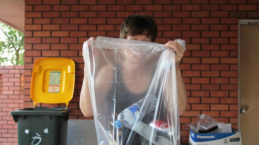 A photo of Glenys Goda holding a transparent bag of rubbish over her head.