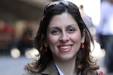 A brunette woman with sunglasses atop her head smiles as she looks into the camera.