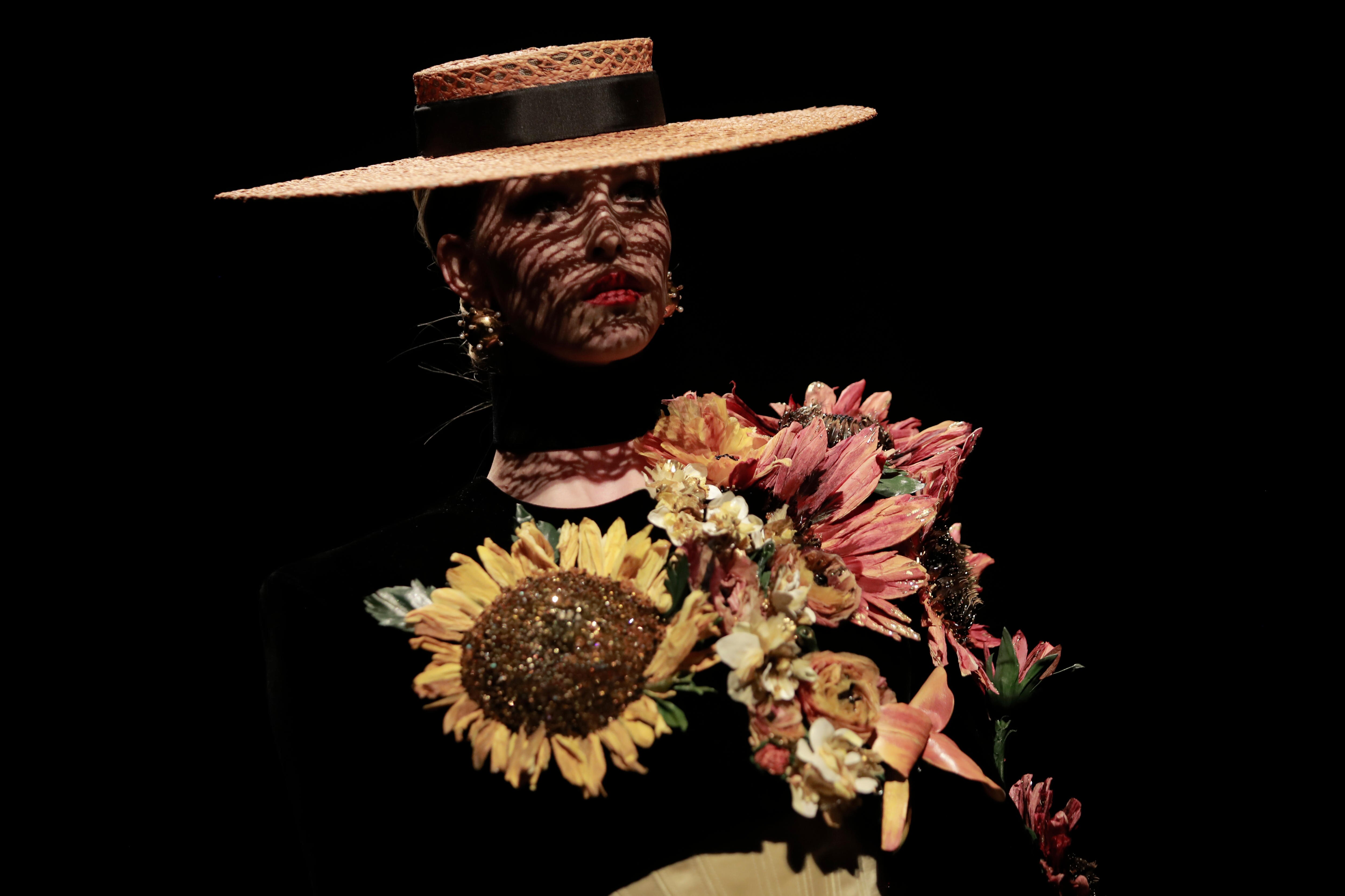 A model wearing a wide brim hat with a shirt covered in flowers. 