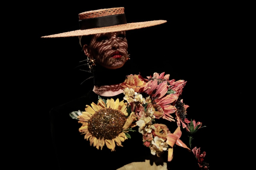 A model wearing a wide brim hat with a shirt covered in flowers. 