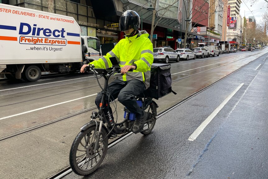 Davis Clayton in high vis jacket and helmet riding a motorbike through a Melbourne street