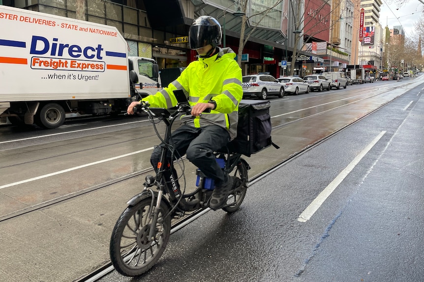 Davis Clayton in high vis jacket and helmet riding a motorbike through a Melbourne street