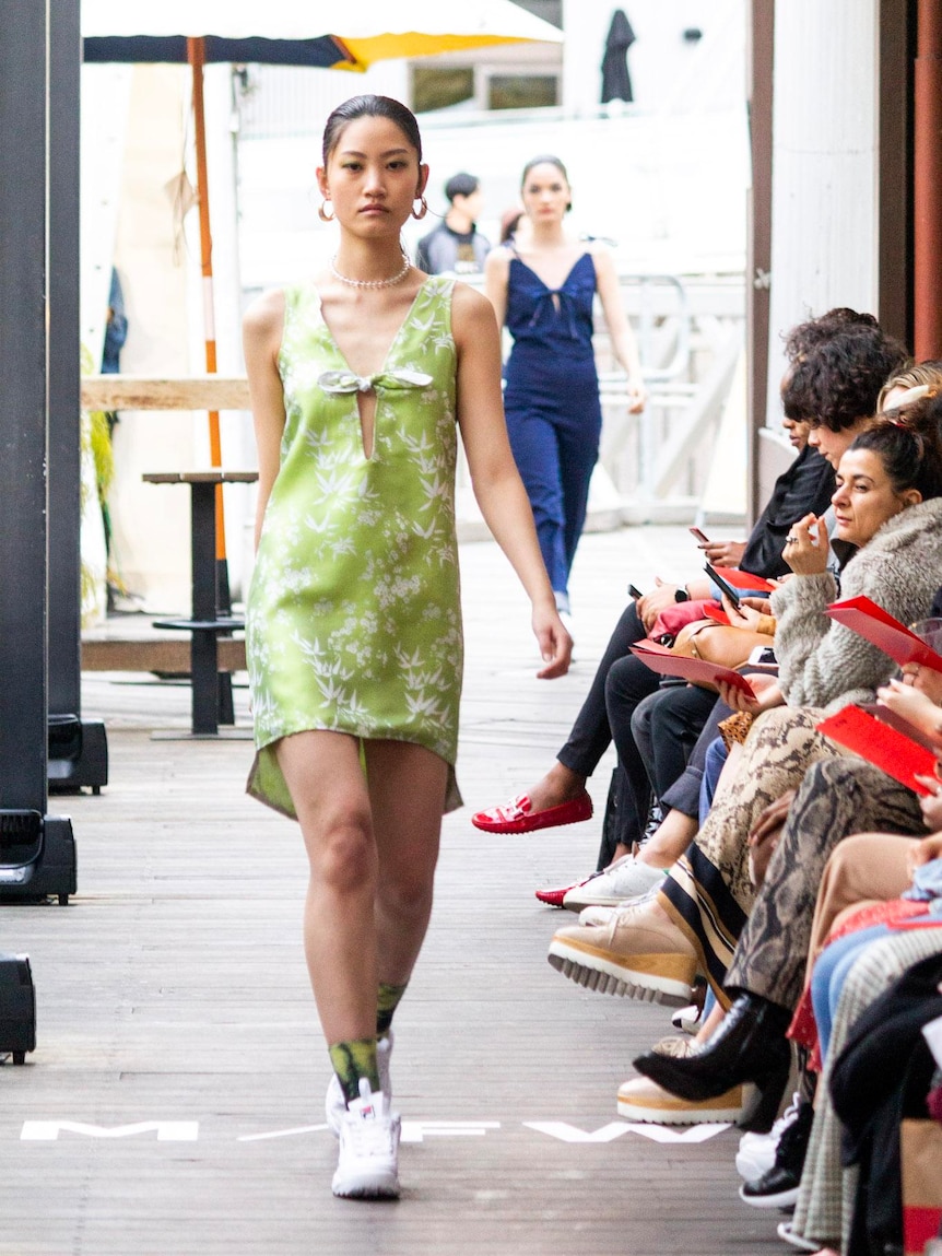 Two models in dresses make their way past a line of seated spectators.