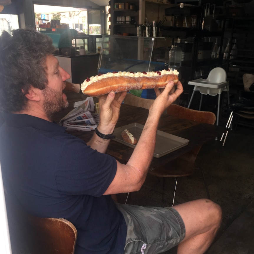 Man holds a large jam and cream doughnut up to his mouth.