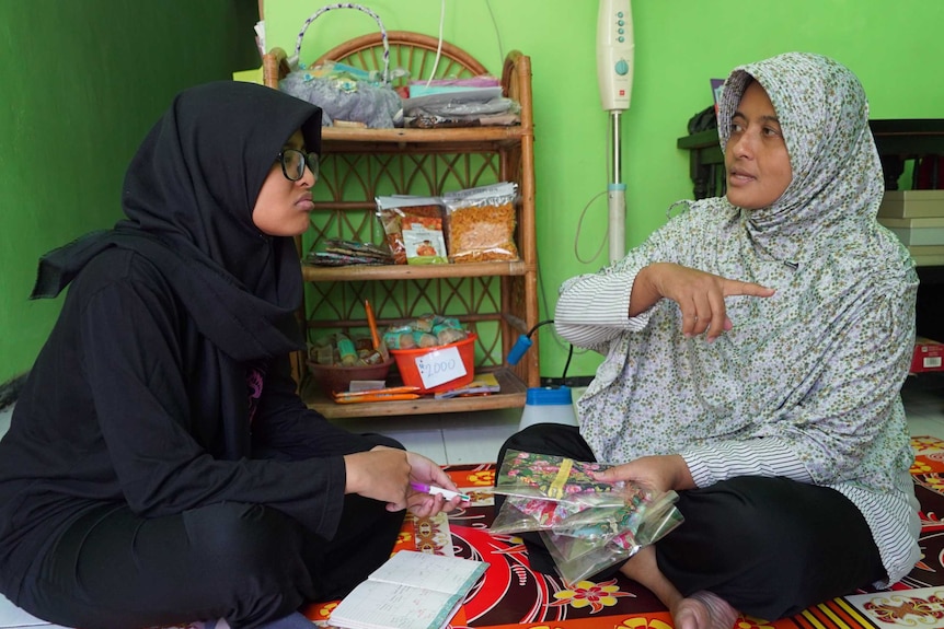 Nur Dhania sits on the floor talking to her mum