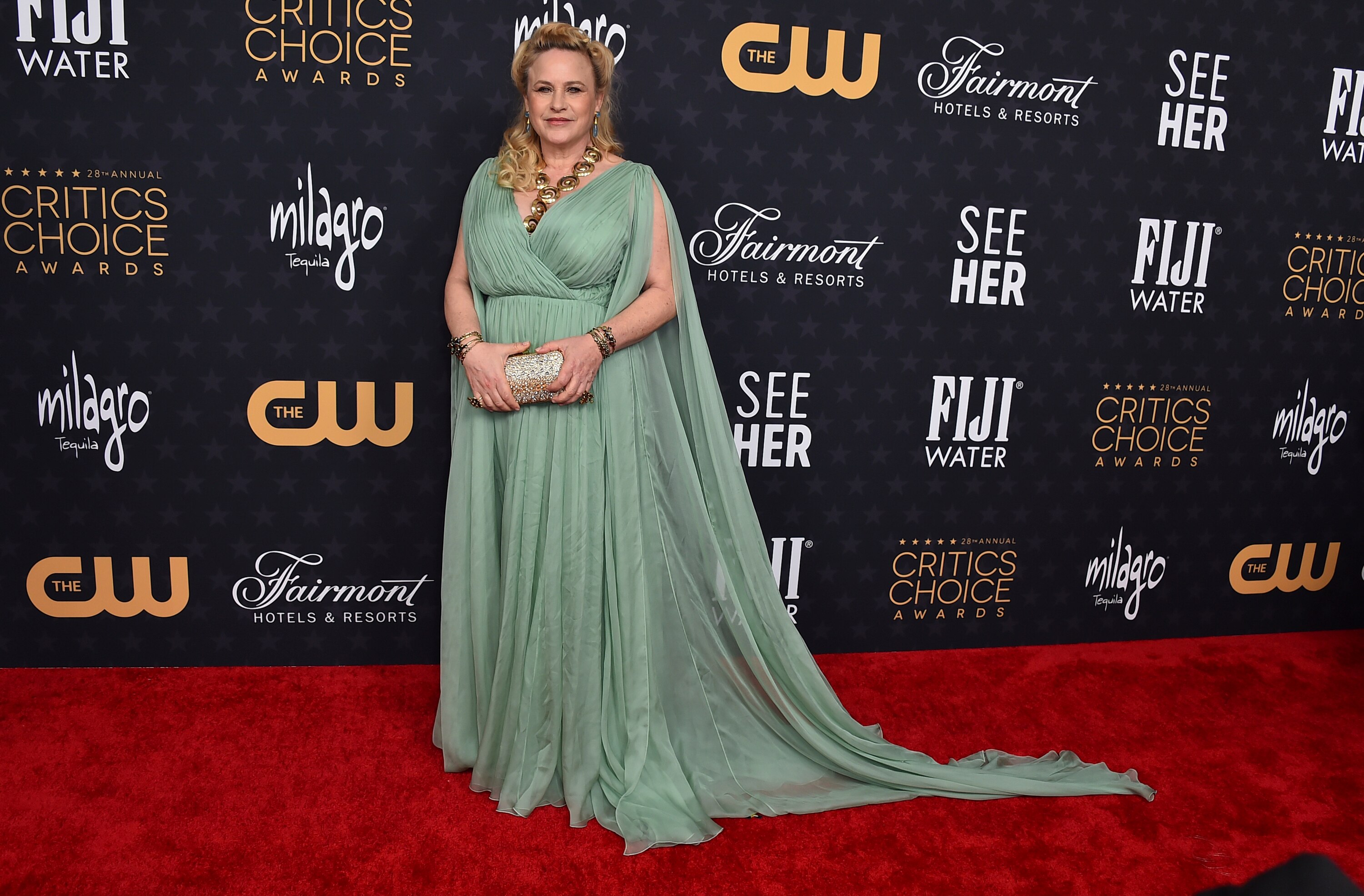 A blond woman in a floor length mint green dress poses for the camera.