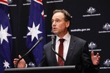 Federal Health Minister Greg Hunt gestures from a podium during a press conference.