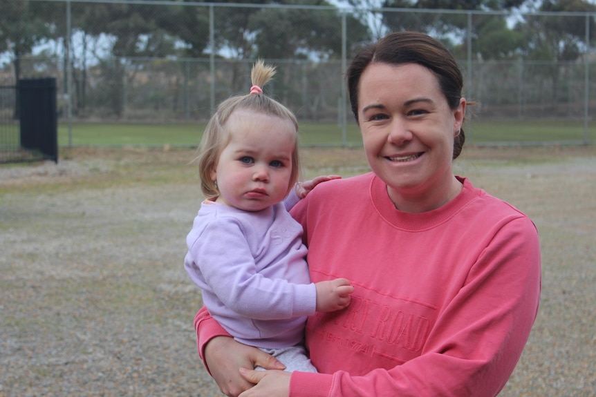 She holds her daughter on her hip and wears a pink jumper