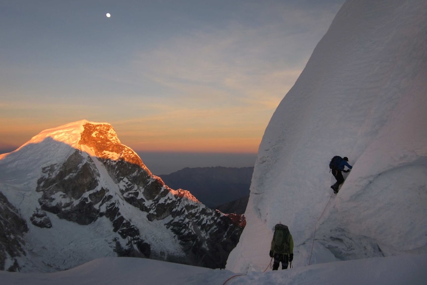 Two people climb a steep, snowy mountain.