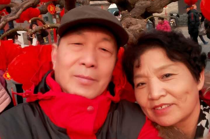 An older man and woman stand under a tree filled with lanterns