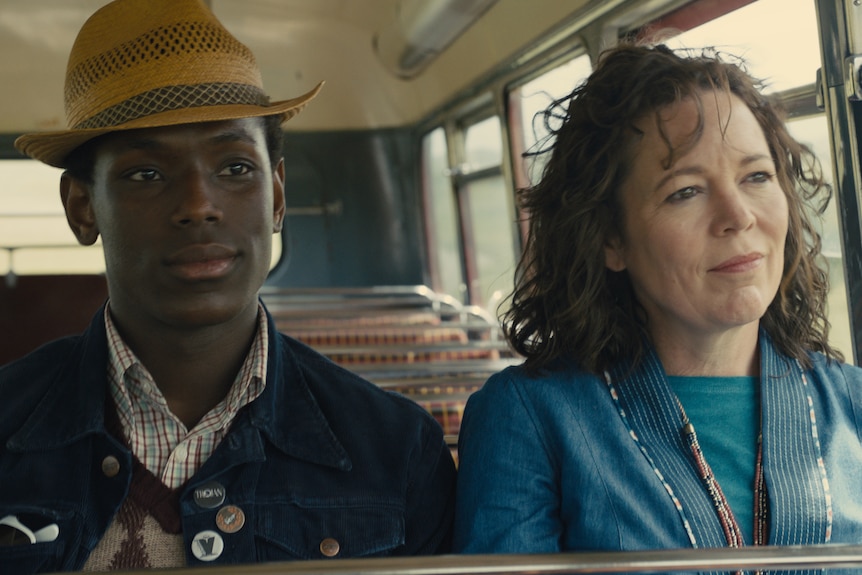 A Black young man and a middle-aged woman sit next to each other on a bus, looking out the window