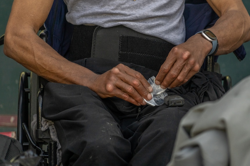 An African American man in a wheelchair holding a small plastic bag with a substance inside.