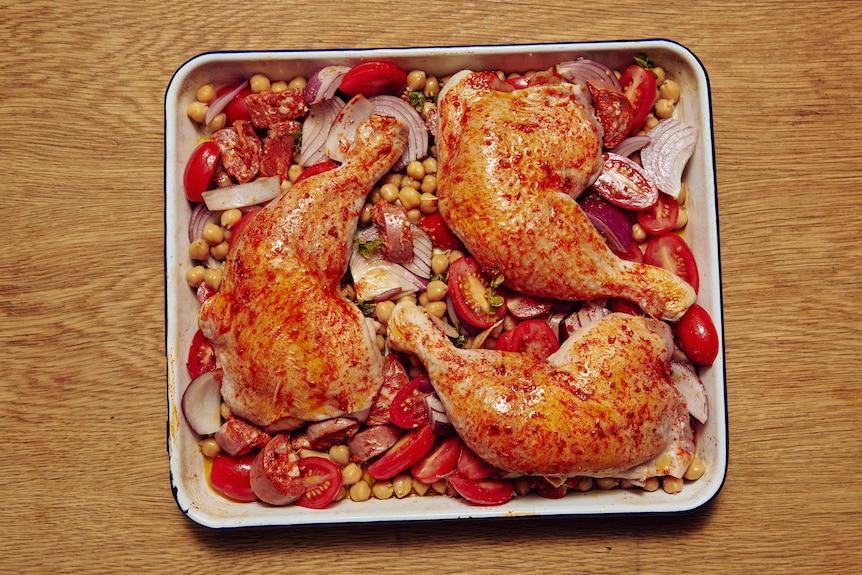 A bird's eye view of a baking tray filled with roast veg, chick peas and roast chicken Marylands.