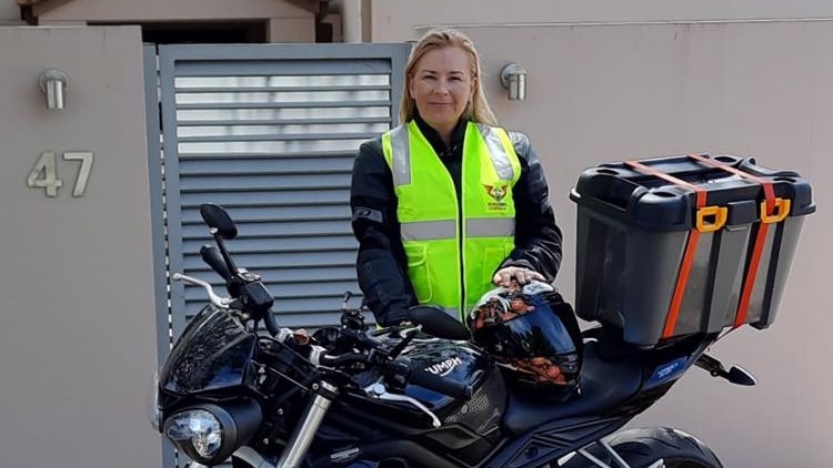 A woman stands behind her motorbike in a yellow vest.