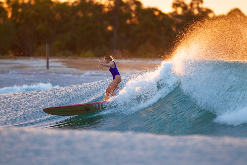 A woman surfing a wave at sunset time