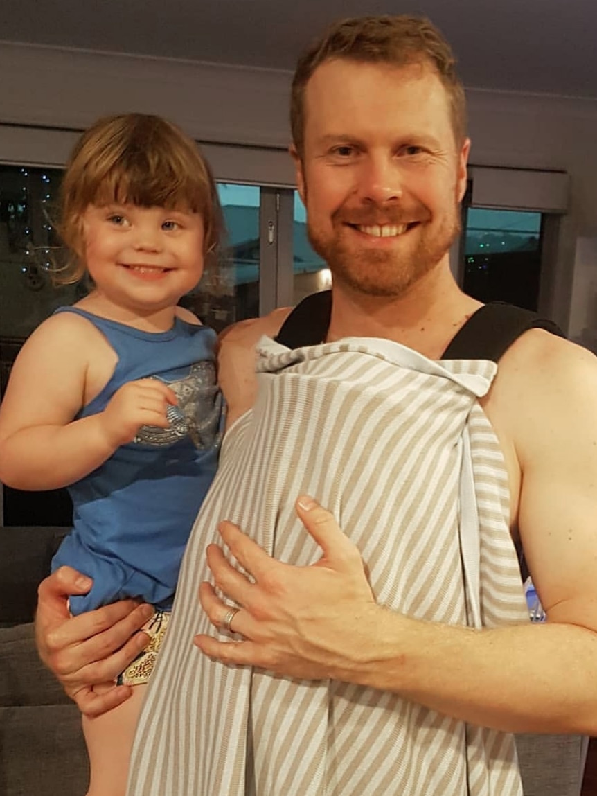 Rob Sturrock holding his smiling daughter and wearing a baby carrier.