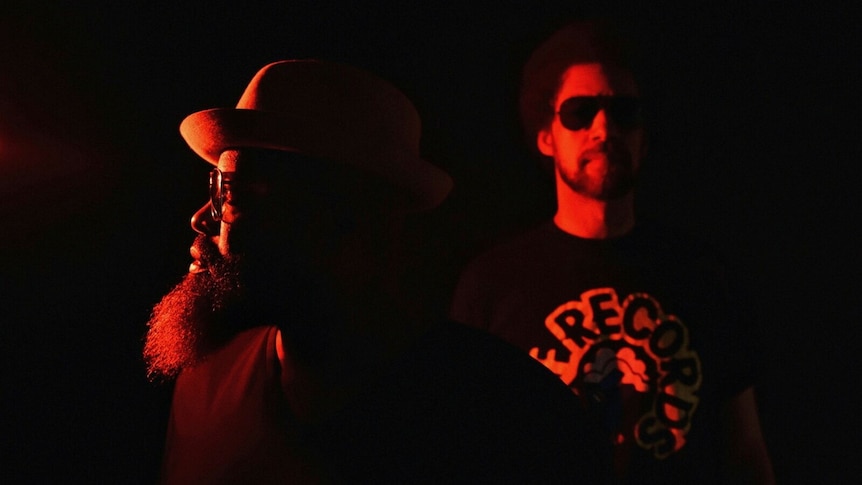 Hip hop artists Danger Mouse and Black Thought stand together bathed in red light