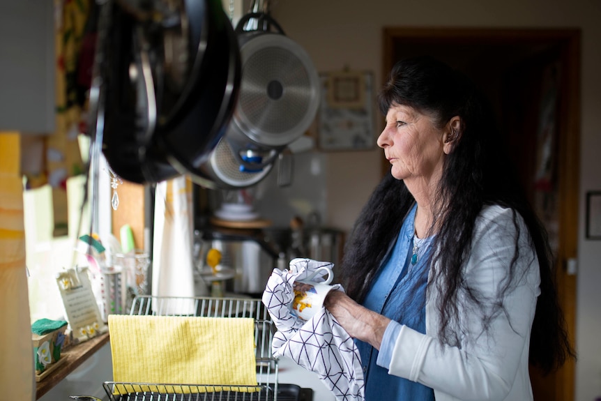 A woman dries dishes looking out her kitchen window