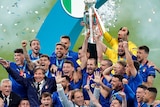 Italy's players and coach stand on the stage and lift the trophy as confetti falls around them