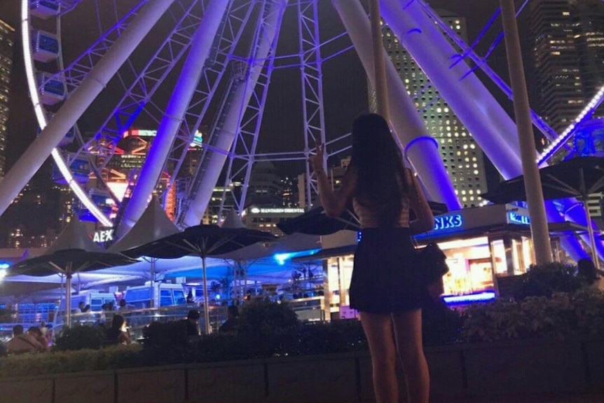Amber Poon Hiu Wing makes a V gesture, back toward camera, at night in Hong Kong. 